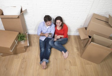 young couple sitting on floor moving in new house using digital 