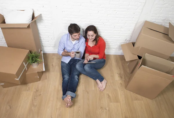 Молода пара сидить на підлозі, рухаючись в новому будинку, використовуючи цифровий — стокове фото