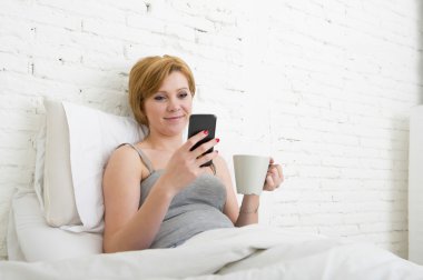 having coffe breakfast on bed while watching internet news in his mobile phone in online communication