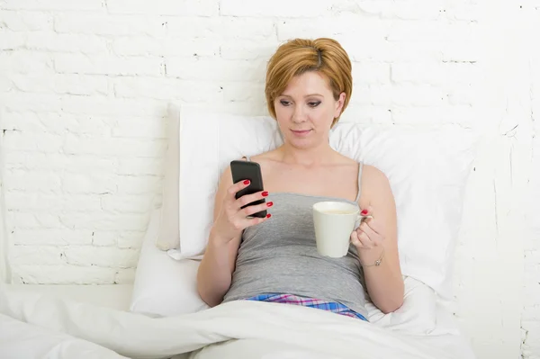 Having coffe breakfast on bed while watching internet news in his mobile phone in online communication — Stockfoto