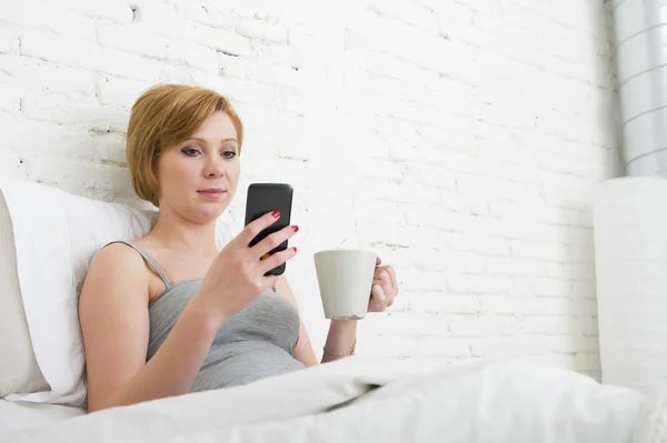 Having coffe breakfast on bed while watching internet news in his mobile phone in online communication — Stockfoto