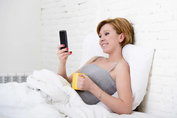 Having coffe breakfast on bed while watching internet news in his mobile phone in online communication — Stok fotoğraf