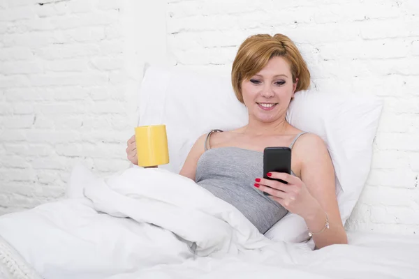 Kaffee frühstücken auf dem Bett, während er Internet-Nachrichten in seinem Handy in der Online-Kommunikation anschaut — Stockfoto