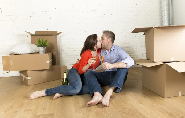 Happy American couple sitting on floor unpacking together celebrating with champagne toast moving in a new house — 图库照片