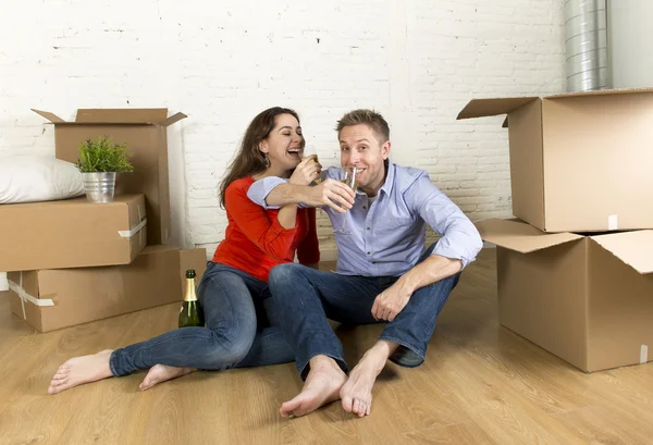 Happy American couple sitting on floor unpacking together celebrating with champagne toast moving in a new house — Stockfoto