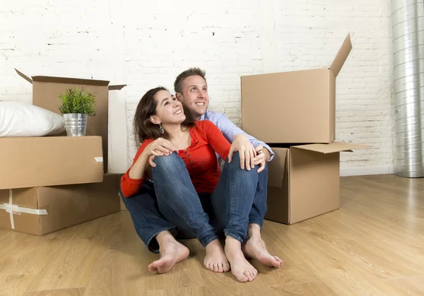 Молодая счастливая пара, сидящая на полу вместе, празднуя переезд в новый дом или квартиру — стоковое фото