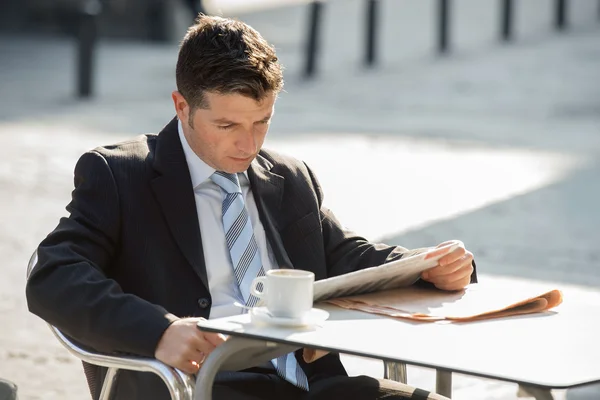 Atractivo hombre de negocios sentado al aire libre tomando una taza de café para desayunar temprano en la mañana leyendo noticias de periódico buscando relajado — Foto de Stock