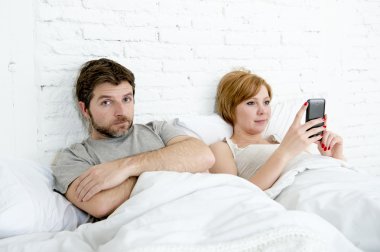 couple in bed husband frustrated upset and unsatisfied while his internet addict wife is using mobile phone