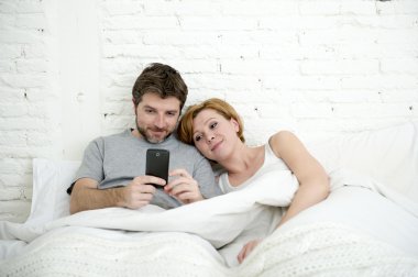 happy attractive couple in bed using mobile phone smiling watching together internet app