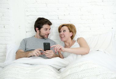 happy attractive couple in bed using mobile phone smiling watching together internet app