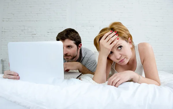 Attraktive Frau, die sich unzufrieden und frustriert im Bett mit ihrem Mann fühlt, während der Mann am Laptop arbeitet und sie ignoriert — Stockfoto