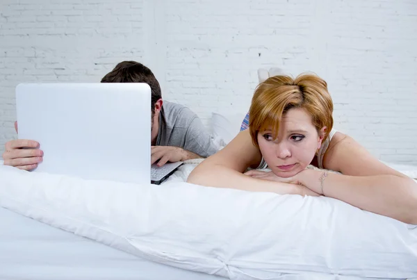 Attraktive Frau, die sich unzufrieden und frustriert im Bett mit ihrem Mann fühlt, während der Mann am Laptop arbeitet und sie ignoriert — Stockfoto