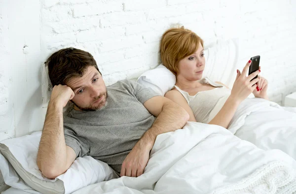 Couple in bed husband frustrated upset and unsatisfied while his internet addict wife is using mobile phone — Zdjęcie stockowe