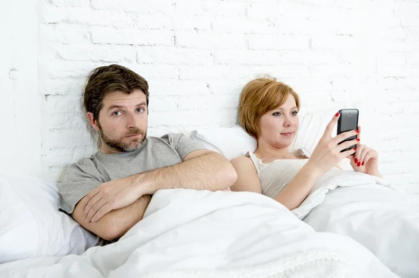 Couple in bed husband frustrated upset and unsatisfied while his internet addict wife is using mobile phone — Stock Photo, Image