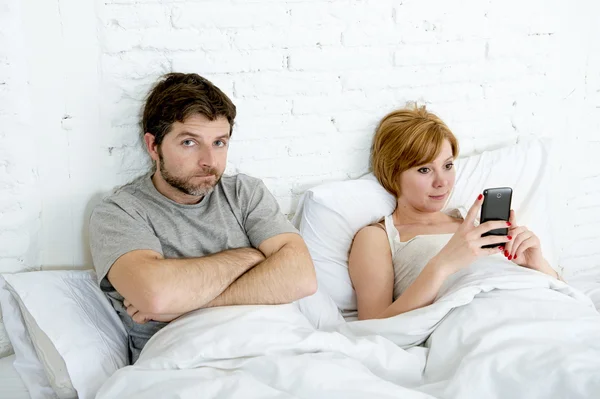 Couple in bed husband frustrated upset and unsatisfied while his internet addict wife is using mobile phone — Stok fotoğraf