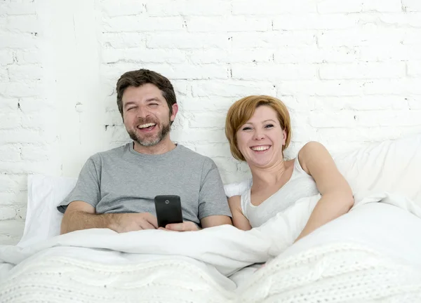 Happy attractive couple in bed using mobile phone smiling watching together internet app — Zdjęcie stockowe