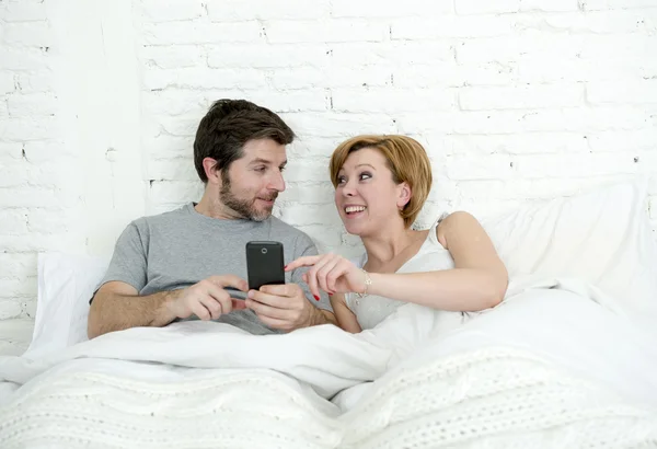 Happy attractive couple in bed using mobile phone smiling watching together internet app — Zdjęcie stockowe
