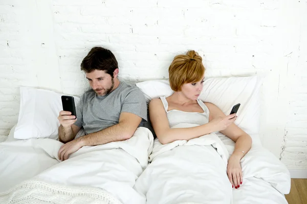 Young couple using mobile phone in bed ignoring each other in relationship communication problems — Stock Photo, Image