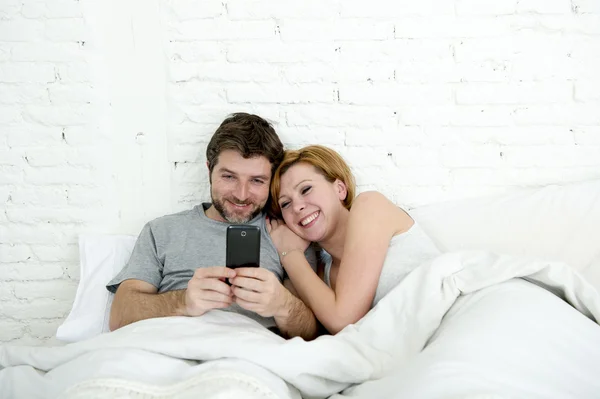 Felice coppia attraente a letto utilizzando il telefono cellulare sorridente guardando insieme internet app — Foto Stock