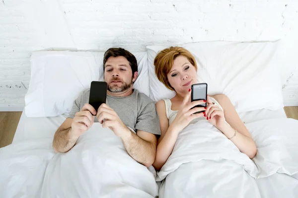 Молода пара використовує мобільний телефон у ліжку, ігноруючи один одного в проблемах спілкування — стокове фото
