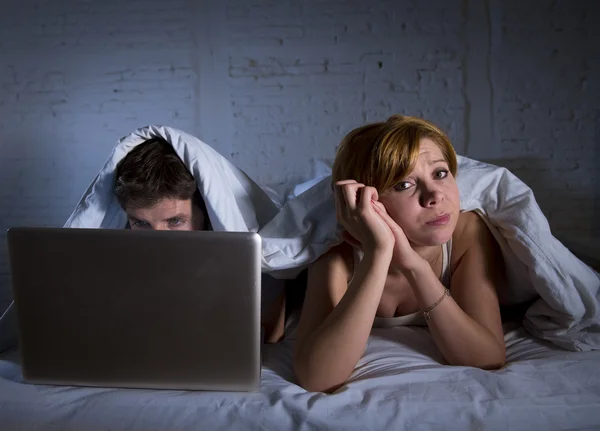 Junge Frau verärgert unzufrieden und frustriert im Bett, während ihr Mann am Laptop arbeitet und sie ignoriert — Stockfoto