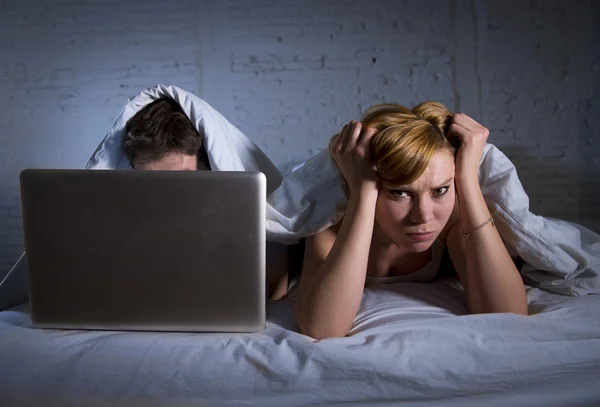 Junge Frau verärgert unzufrieden und frustriert im Bett, während ihr Mann am Laptop arbeitet und sie ignoriert — Stockfoto