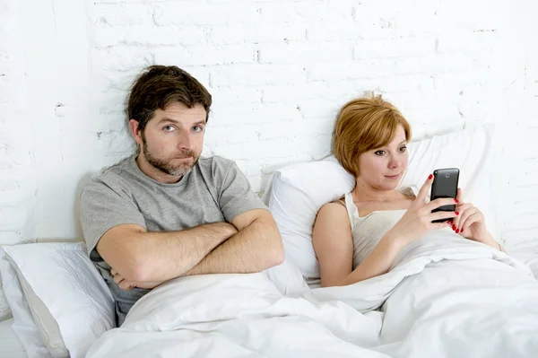 Couple in bed husband frustrated upset and unsatisfied while his internet addict wife is using mobile phone — Stock Photo, Image
