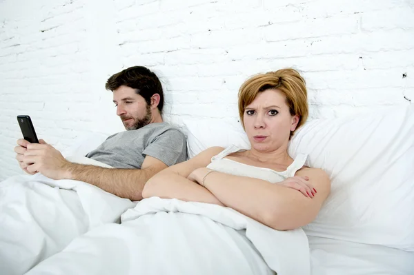 Young couple in bed unsatisfied wife bored frustrated and angry while internet addict husband is using mobile phone  social network obsession — Stock Photo, Image