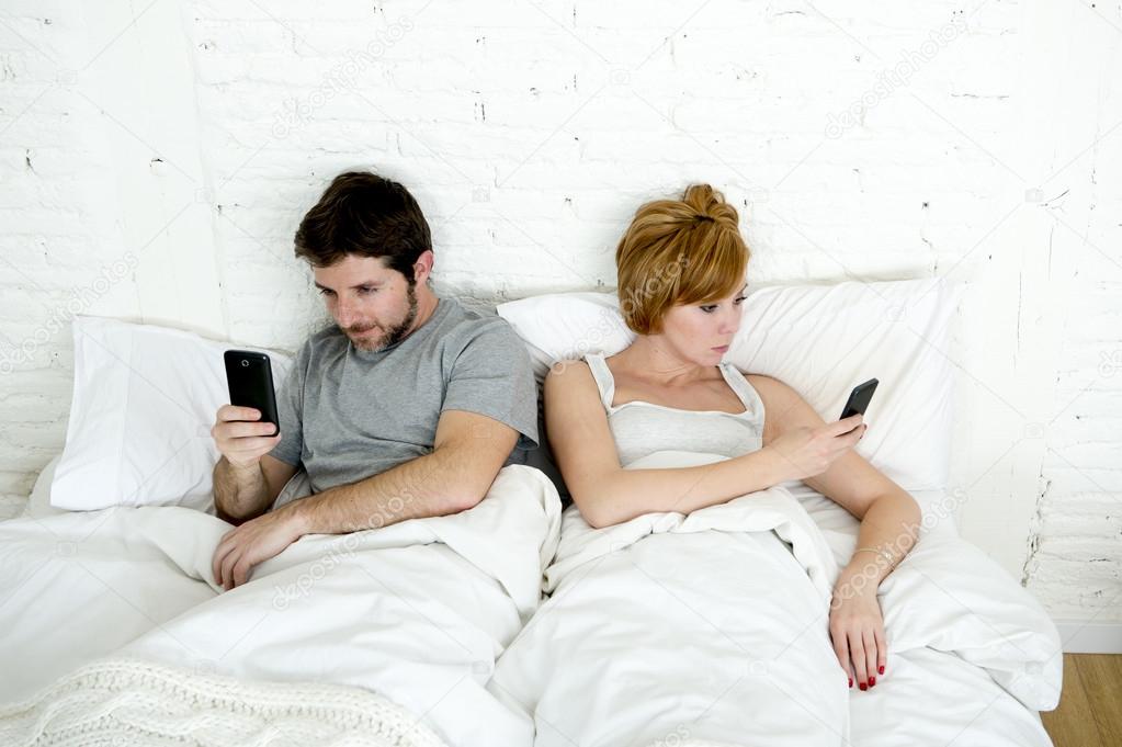 young couple using mobile phone in bed ignoring each other in relationship communication problems