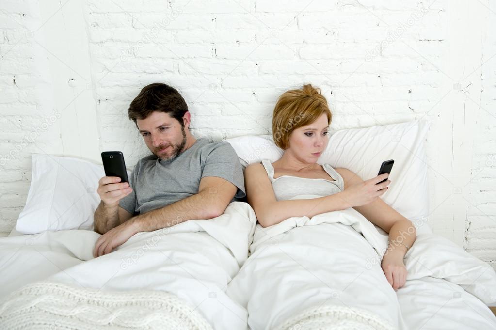 young couple using mobile phone in bed ignoring each other in relationship communication problems