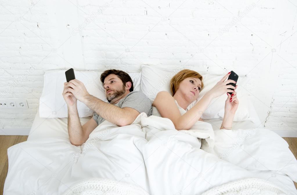 young married couple using their mobile phone in bed ignoring each other in relationship communication problems