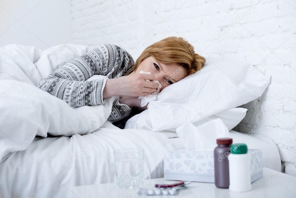 woman with sneezing nose blowing in tissue on bed suffering cold flu virus symptoms having medicines tablets pills