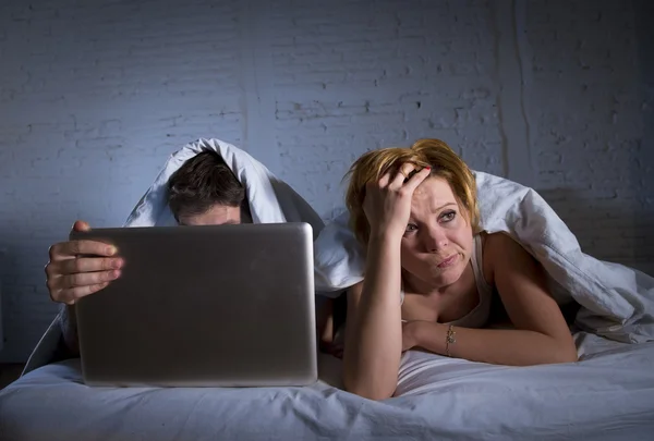 不満と彼女を無視してコンピューターのラップトップ上の夫仕事しながらベッドで不満の若い妻を混乱させる — ストック写真