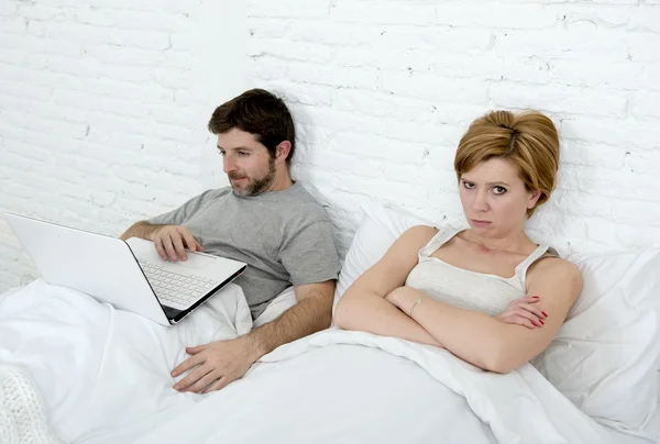 有魅力的女人感觉沮丧不满和沮丧在床上与他丈夫而忽略她的笔记本电脑的人工作 — 图库照片