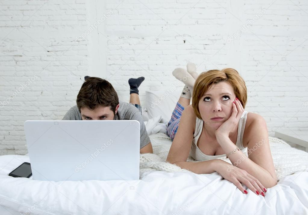 attractive woman feeling upset unsatisfied and frustrated in bed with his husband while the man work on computer laptop ignoring her