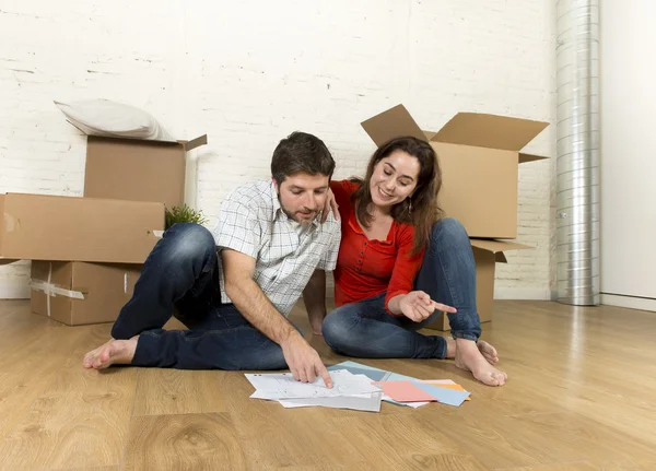 Happy American couple sitting on floor moving in new house looking blueprints — Stock Photo, Image