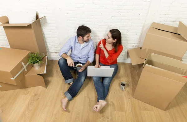 Пара сидить на підлозі, рухаючись в новому будинку, вибираючи меблі з комп'ютерним ноутбуком — стокове фото