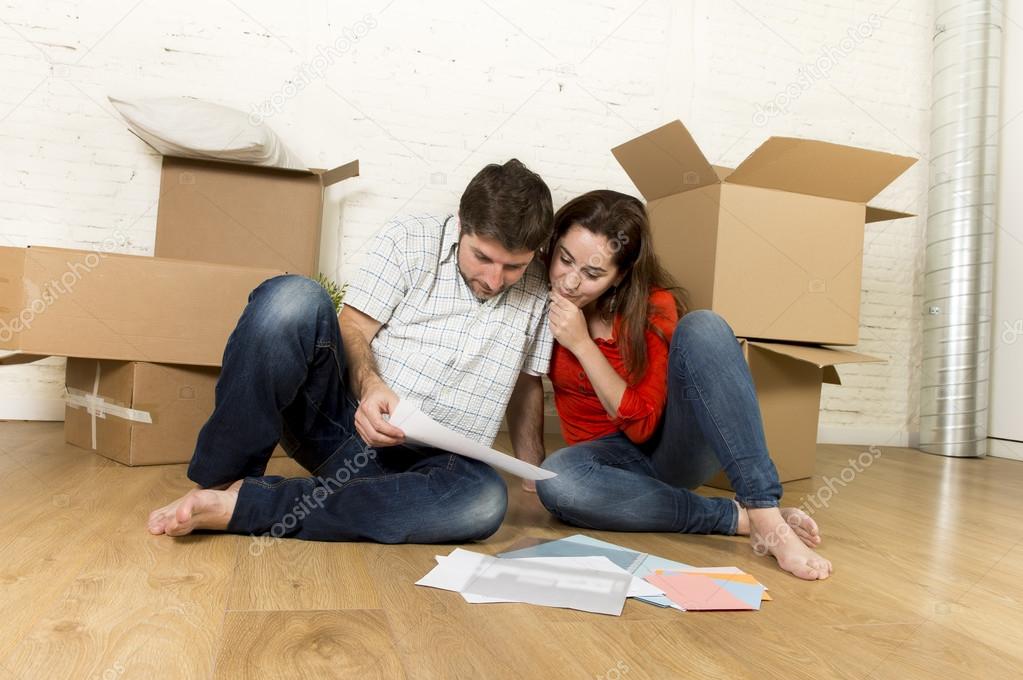 happy American couple sitting on floor moving in new house looking blueprints 