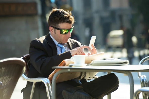 Uomo d'affari in occhiali da sole che fa colazione caffè leggendo giornale utilizzando internet sul telefono cellulare — Foto Stock