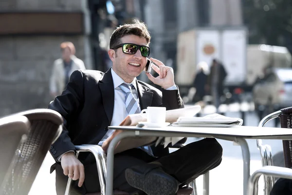 Επιχειρηματία σε γυαλιά ηλίου έχοντας πρωινό καφέ νωρίς το πρωί διαβάζοντας εφημερίδα νέα μιλάμε για κινητό τηλέφωνο — Φωτογραφία Αρχείου