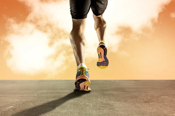 Сильные спортивные ноги с разорванной телячьей мышцей молодого спортсмена, бегущего по гранж асфальтовой дороге на оранжевом небе заката — стоковое фото