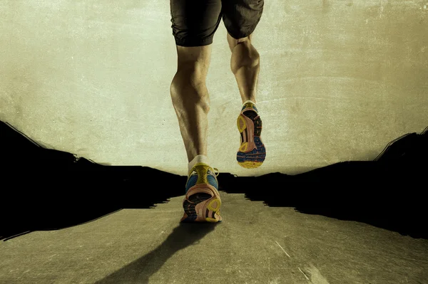 Fuertes piernas atléticas con el músculo de la pantorrilla rasgado del joven deportista corriendo en el camino de asfalto grunge — Foto de Stock