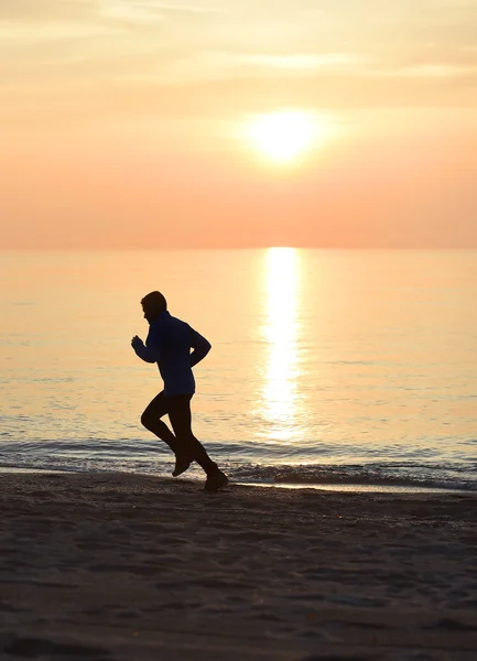 실루엣이라는 젊은 운동 선수가 해질 무렵 오렌지 하늘을 배경으로 해변을 뛰어다니고 있다 — 스톡 사진