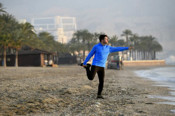 Junger Sportler beim Stretching, bevor er am frühen Morgen am Strand vor dem Meer joggt — Stockfoto