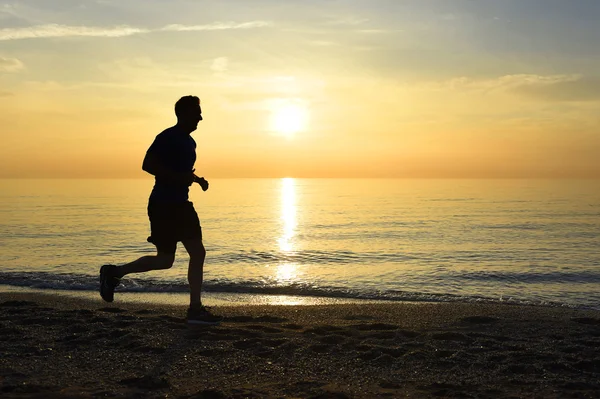 Silhouette junger Sportler läuft draußen am Strand bei Sonnenuntergang mit orangefarbenem Himmel — Stockfoto