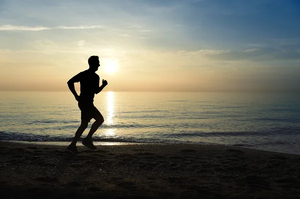 Silhouette joven deportista corriendo al aire libre en la playa al atardecer con cielo naranja — Foto de Stock