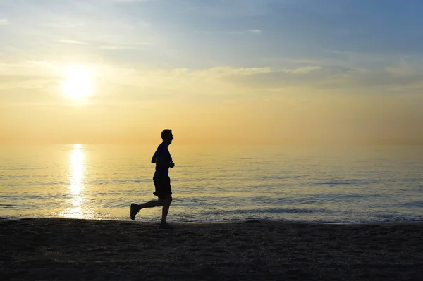Silhouette giovane uomo sportivo correre all'aperto sulla spiaggia al tramonto cielo arancione — Foto Stock
