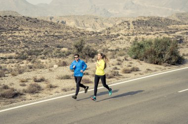 attractive sport couple man and woman running together on desert asphalt road mountain landscape