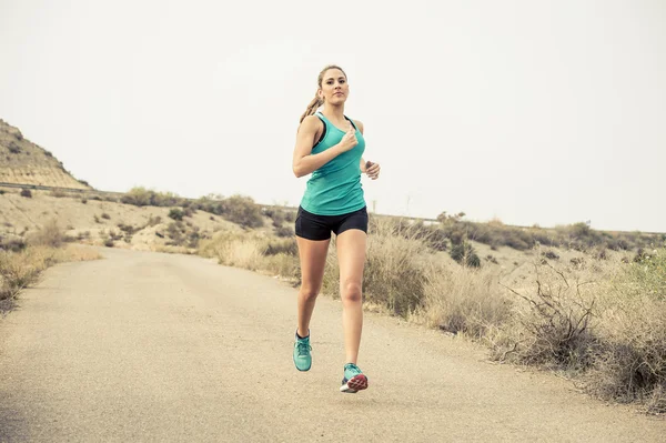 Sportlerin läuft auf Asphalt schmutzige Straße mit trockener Wüstenlandschaft Hintergrundtraining hart — Stockfoto