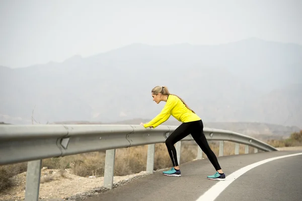 Olahraga wanita meregangkan otot kaki setelah menjalankan latihan di jalan aspal dengan lanskap gurun kering dalam sesi pelatihan kebugaran yang sulit — Stok Foto